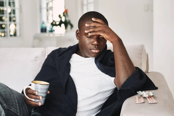 Mężczyzna siedzący na kanapie w domu pije tabletki na ból głowy. — Zdjęcie stockowe