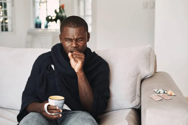 Seorang pria dingin duduk di sofa dengan minuman panas — Stok Foto