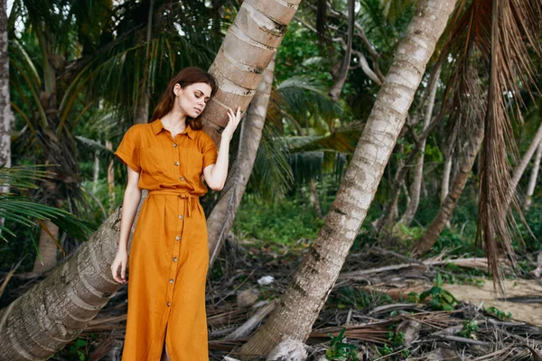 A mulher jovem em um sundress toca um tronco de uma palmeira em uma natureza — Fotografia de Stock