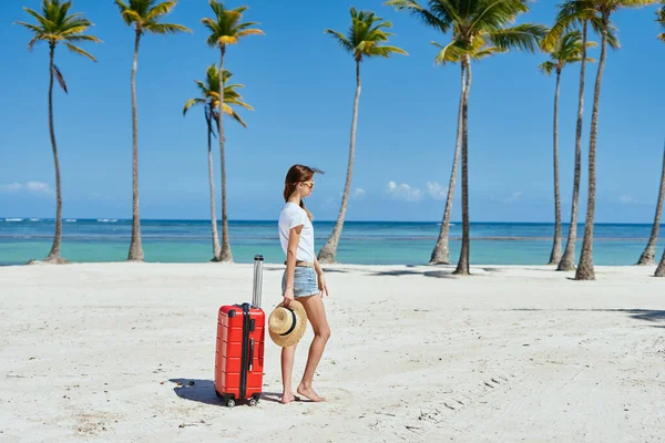 Una mujer encantadora con una maleta roja en una isla — Foto de Stock