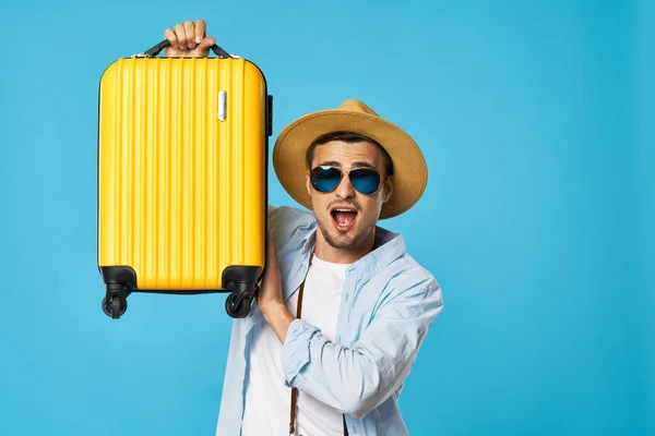 Hombre sobre un fondo azul con gafas y una maleta amarilla — Foto de Stock