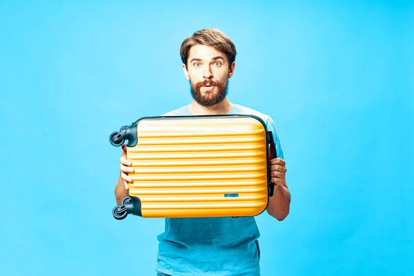 Hombre guapo con una maleta amarilla sobre un fondo azul sorpresa — Foto de Stock