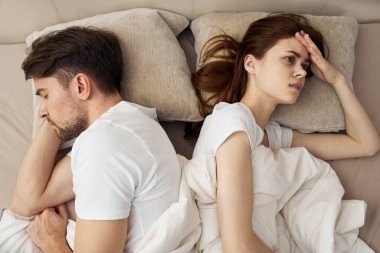 An upset woman lies in bed and the man next to her clipart