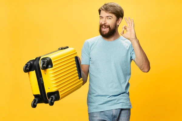Handsome man with a golden suitcase shows a positive gesture and winks — Stock Photo, Image