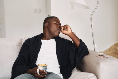 Kanepede Afrikalı bir adam ve sıcak bir içecekle birlikte bir hap bardağı.