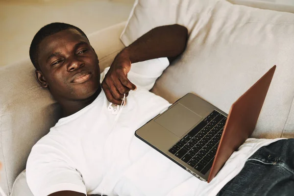 Симпатичный парень лежит на диване с ноутбуком и смотрит — стоковое фото