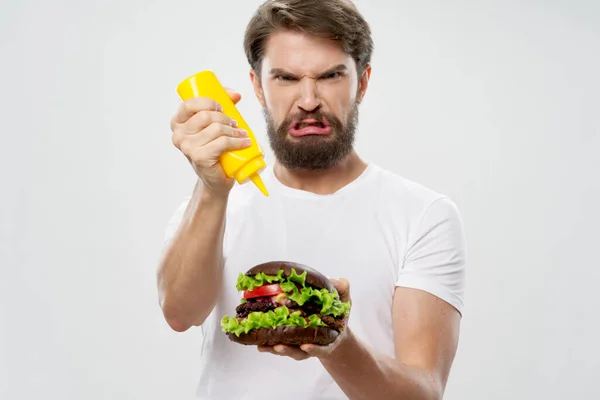 Zły człowiek z obrzydzeniem trzyma hamburgera i musztardę — Zdjęcie stockowe