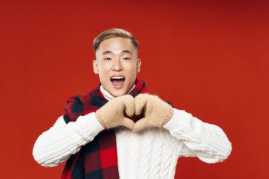  Kırmızı arka plandaki adam elleri ve kalın giysileriyle bir kalp gösteriyor.