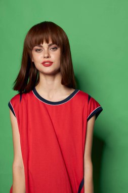 Kırmızı tişörtlü kadın yeşil arka plandaki kameraya bakıyor.