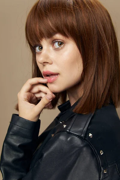Ung vacker kvinna poserar på en beige bakgrund i studion i en svart läderjacka — Stockfoto