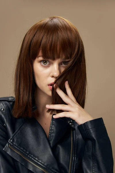 Joven hermosa mujer posando sobre un fondo beige en el estudio en una chaqueta de cuero negro —  Fotos de Stock