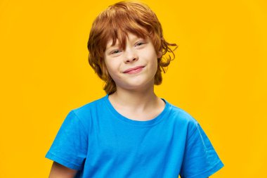 Smiling redhead boy close-up blue t-shirt yellow background clipart