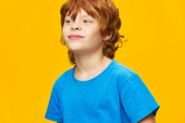 Chłopiec odwraca wzrok niebieski t-shirt żółty tło czerwone włosy — Zdjęcie stockowe