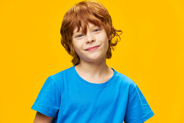 Smiling redhead boy close-up blue t-shirt yellow background