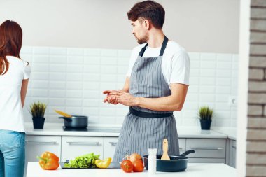 Mutfakta önlüklü bir şef, taze sebzeler ve kot pantolonlu bir kadın. 