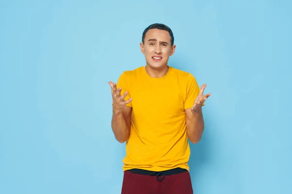 Mann im gelben T-Shirt gestikuliert mit den Händen auf blauem Hintergrund — Stockfoto
