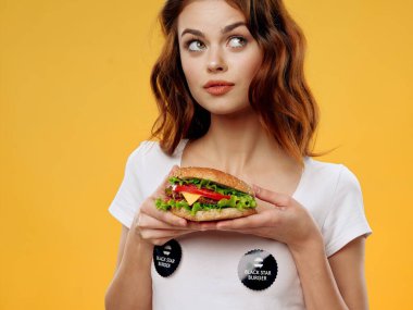 Sebzeli hamburger ve tişörtlü endişeli bir kadın. 