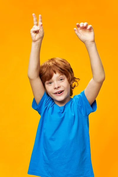 Alegre menino mãos levantadas azul t-shirt amarelo fundo vermelho cabelo — Fotografia de Stock