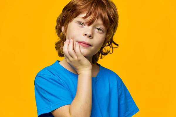 Niño pelirrojo con una camiseta azul fondo amarillo, sostiene una mano cerca de su cara — Foto de Stock