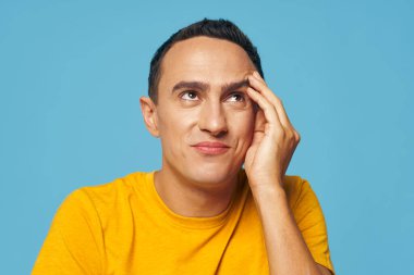 Duygusal bir adam elini yüzüne yakın tutar. Öfke, asık sarı tişört.