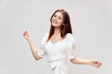 Beyaz elbiseli esmer, gülümseyen, el kol hareketi yapan gri arkaplan..