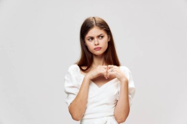 Beyaz elbiseli bir esmer ellerini onun önünde tutuyor ve yan tarafa bakıyor. 