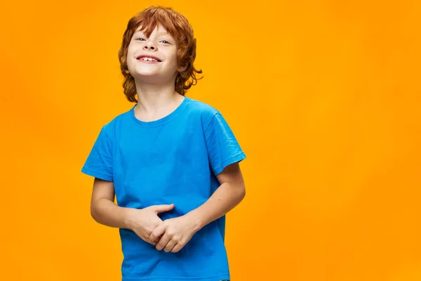 黄色の背景に青いTシャツを着た幸せな少年が手を携えています — ストック写真