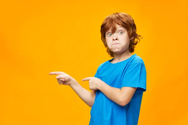 Surprised red-haired child points to the side and blue T-shirt — Stock Photo, Image