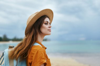 Sırt çantalı gezgin doğa adası manzarasında şapka takıyor. 