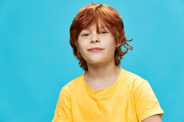 Glad pojke med rött hår i en gul t-shirt på en blå bakgrund — Stockfoto