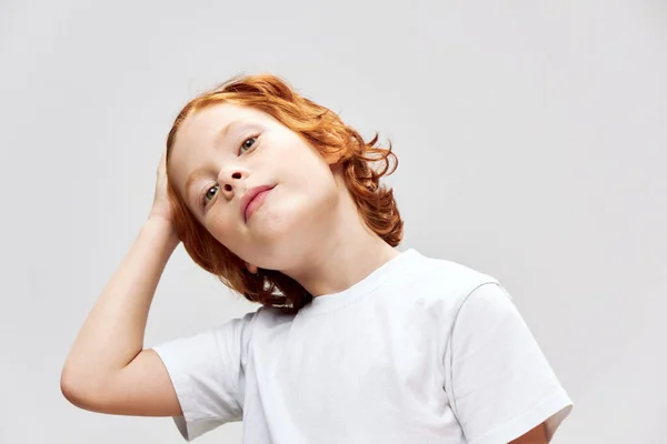 Schattige roodharige jongen houdt zijn hand op zijn hoofd wit t-shirt bijgesneden uitzicht — Stockfoto