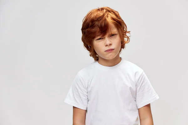 Displeased red-haired boy squints his eyes white t-shirt incredulous look — Stock Photo, Image