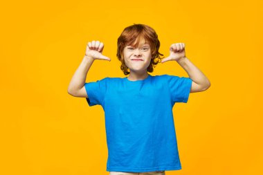 Kızıl saçlı çocuk kameraya surat asıyor ve elleriyle işaret ediyor. Kızgın yüz ifadesi duyguları. 