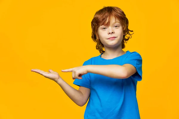 Rödhårig pojke på en gul bakgrund pekar fingret åt sidan och fritt utrymme — Stockfoto