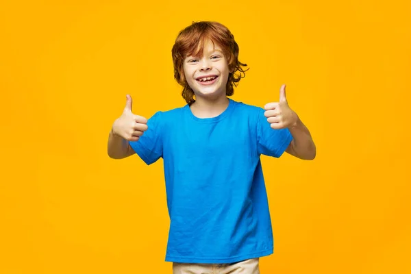 Vidám gyerek kék pólóban mutatja a hüvelykujját, és jól érzi magát — Stock Fotó