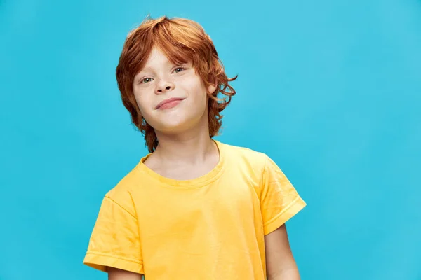 Рыжий ребенок улыбается на синем фоне и в желтой футболке — стоковое фото