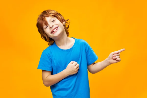 Criança feliz em uma camiseta azul aponta para o lado e sorri — Fotografia de Stock