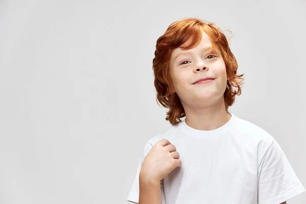 Rolig rödhårig pojke leende vit t-shirt beskärd vy grå isolerad bakgrund — Stockfoto