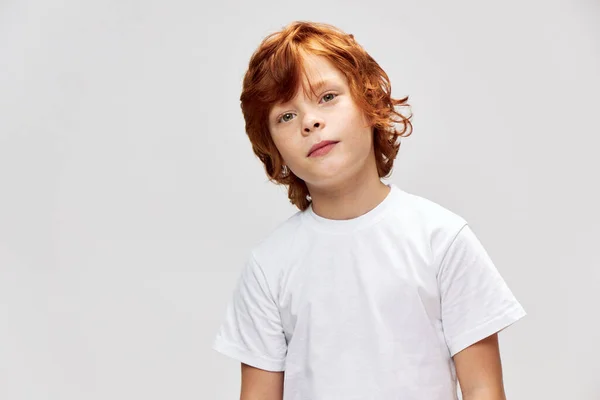 Niño pelirrojo con una camiseta blanca inclinó la cabeza hacia un lado rojo — Foto de Stock