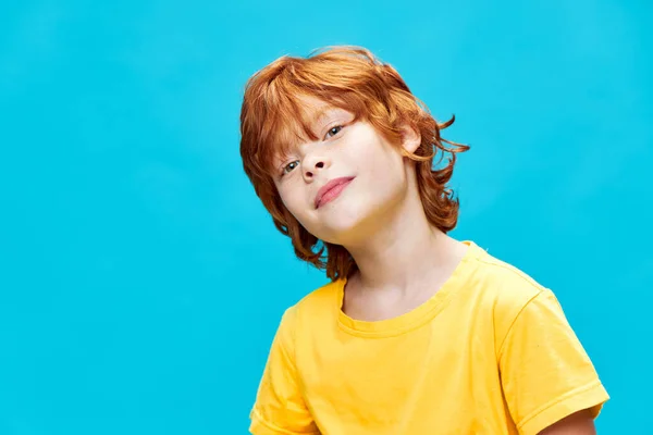 Un niño pelirrojo con una camiseta amarilla inclinó su cabeza hacia un lado contra —  Fotos de Stock