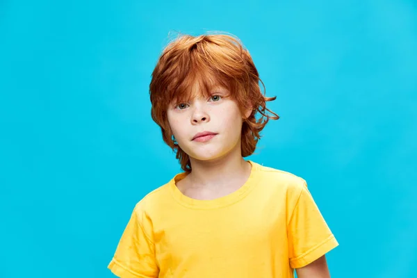 Söt pojke med rött hår på en isolerad bakgrund i en gul t-shirt — Stockfoto