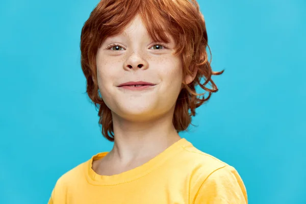 Retrato de um menino de cabelos vermelhos sorridente em uma camiseta amarela em um fundo azul — Fotografia de Stock