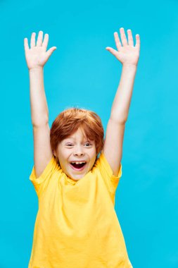 Mutlu kızıl saçlı çocuk, kaldırılmış kollarıyla gülüyor ve mavi