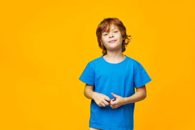 Kamera stüdyosuna gülümseyen kızıl saçlı çocuk sarı izole bir arka plan çekmiş. 