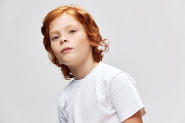 Beyaz tişörtlü kızıl saçlı çocuk yakın çekimde kırpılmış gri arka plan 
