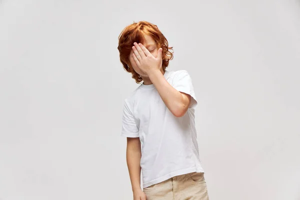 Red-haired boy mortgage near face in white t-shirt gray background — Stock Photo, Image