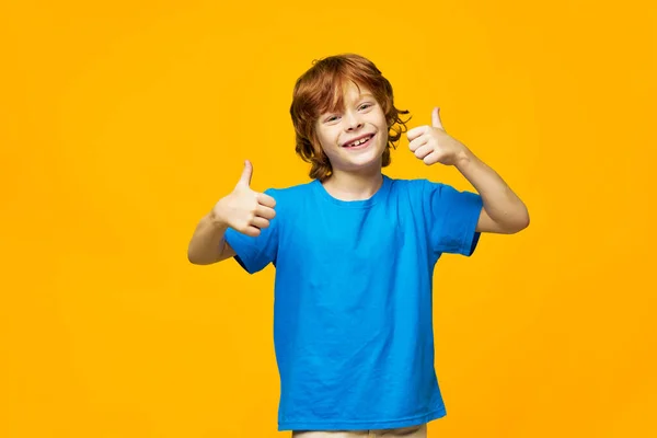 Jongen rood haar blauw t-shirt geel geïsoleerde achtergrond sproeten en een vrolijke blik van de duim — Stockfoto