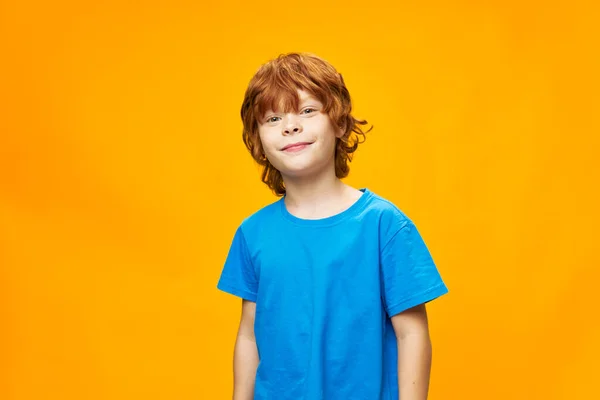 Chłopiec rude włosy niebieski t-shirt żółty pojedyncze tło piegi i piękny uśmiech dzieci wygląd — Zdjęcie stockowe