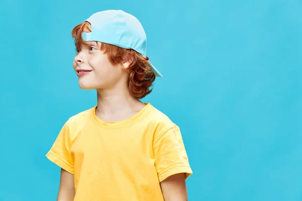 Рыжий ребенок в кепке на синем фоне смеется — стоковое фото