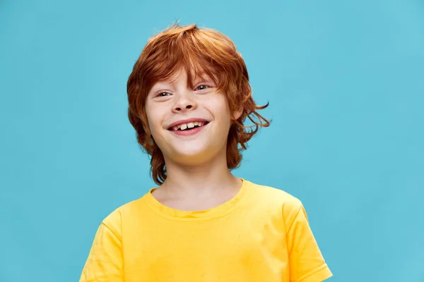Glad barn i en gul t-shirt på en blå bakgrund leende — Stockfoto